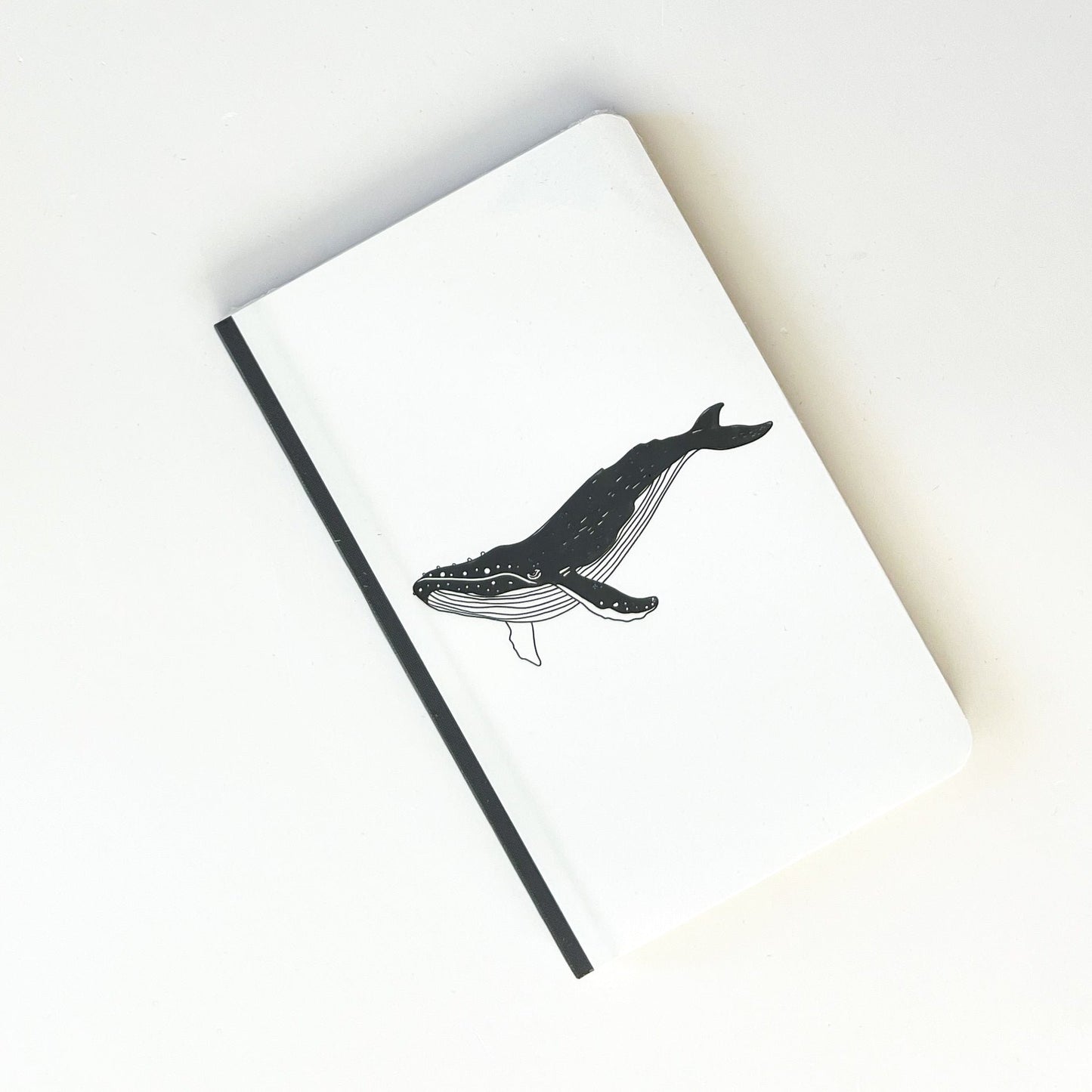 Foto de libreta chica con dibujo de ballena en negro, lomo negro con fondo