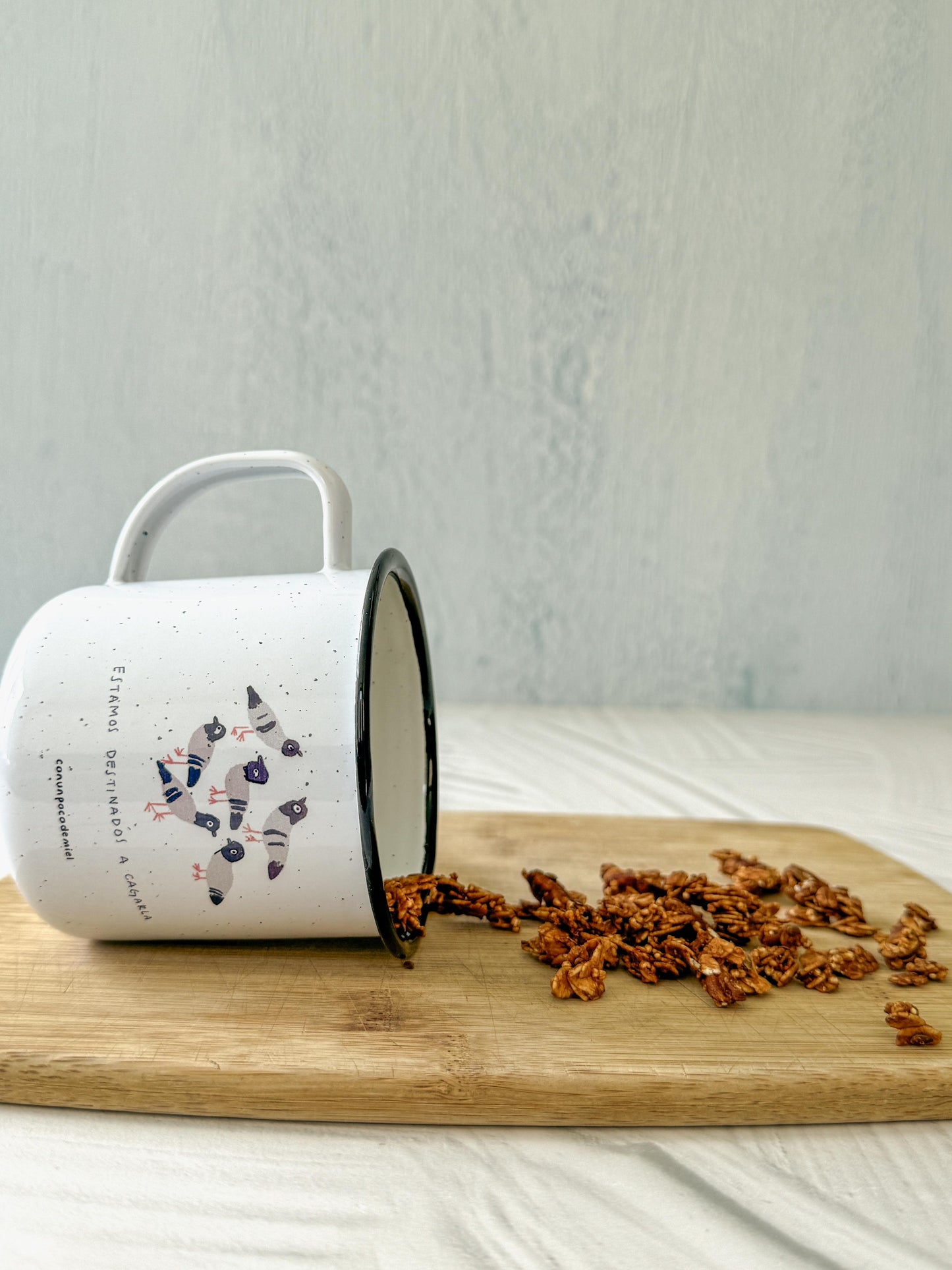 Taza de peltre con dibujo de palomas y texto estamos destinados a cagarla en tabla de madera con granola
