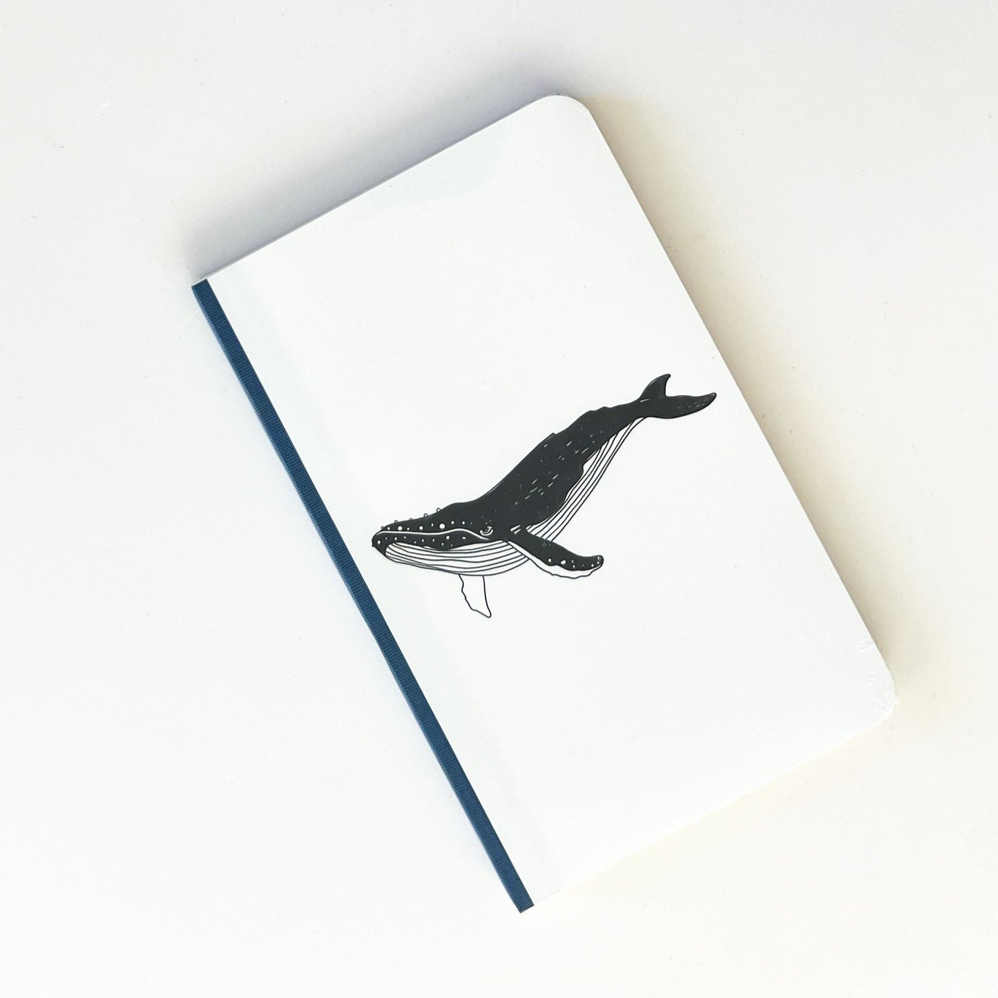 Foto de libreta chica con dibujo de ballena en negro, lomo azul